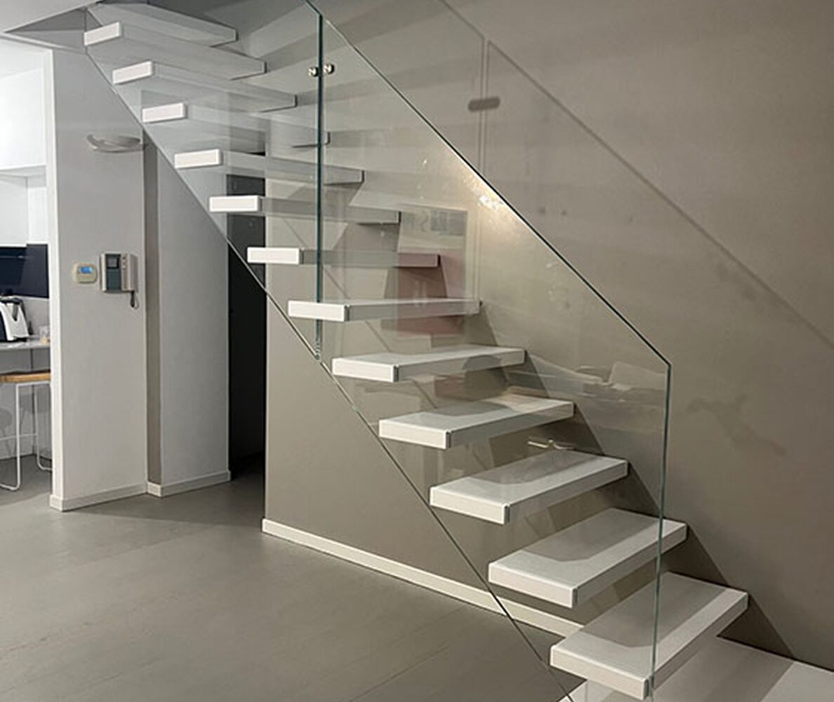 Scala sospesa con gradini bianchi, corrimano in vetro e parapetto in vetro su parete grigia in ambiente moderno